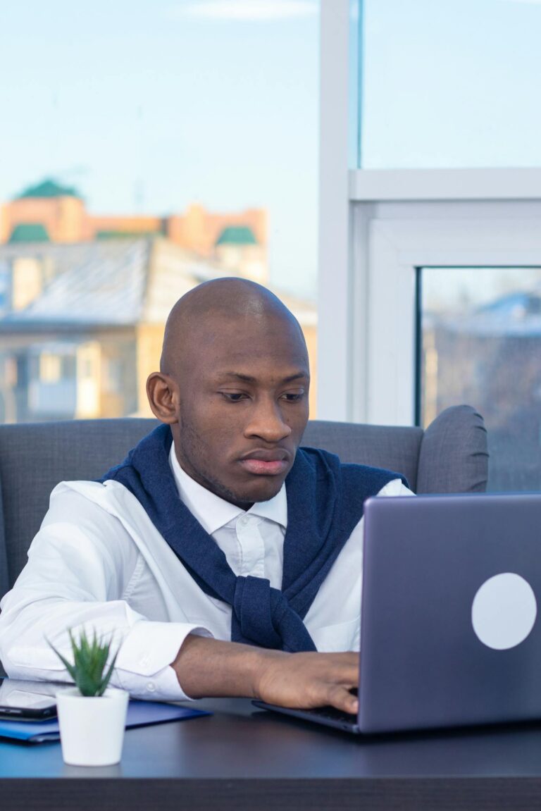 Business professional concentrating on work at a laptop in a modern office with a city view.